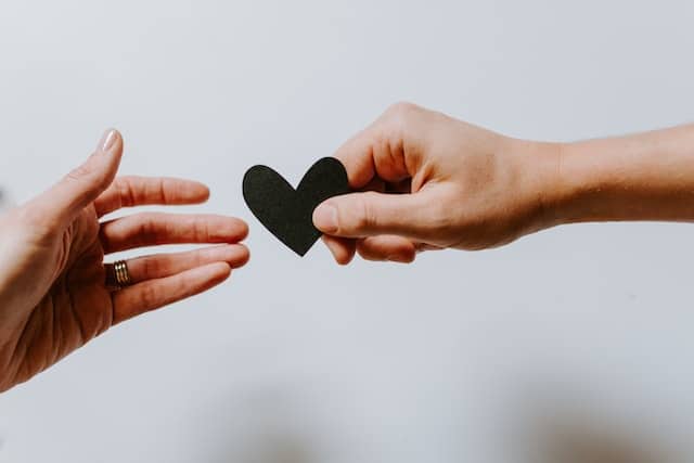 A hand holding out a paper heart to another hand. Here are some ideas to celebrate random acts of kindness day