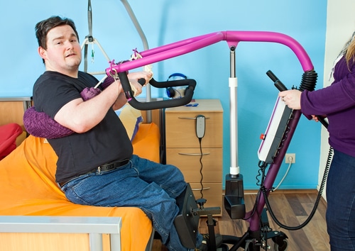 A young man with infantile cerebral palsy using a patient lift to hoist himself out of a healthcare bed