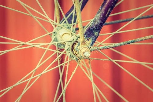 A close-up of a bicycle wheel. The wheel is made of metal and has spokes that radiate out from the center. The wheel is attached to a bicycle frame.