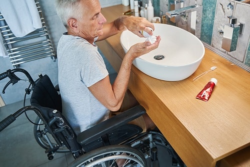spina bifida affects this grey haired man in a wheelchair at the bathroom sink