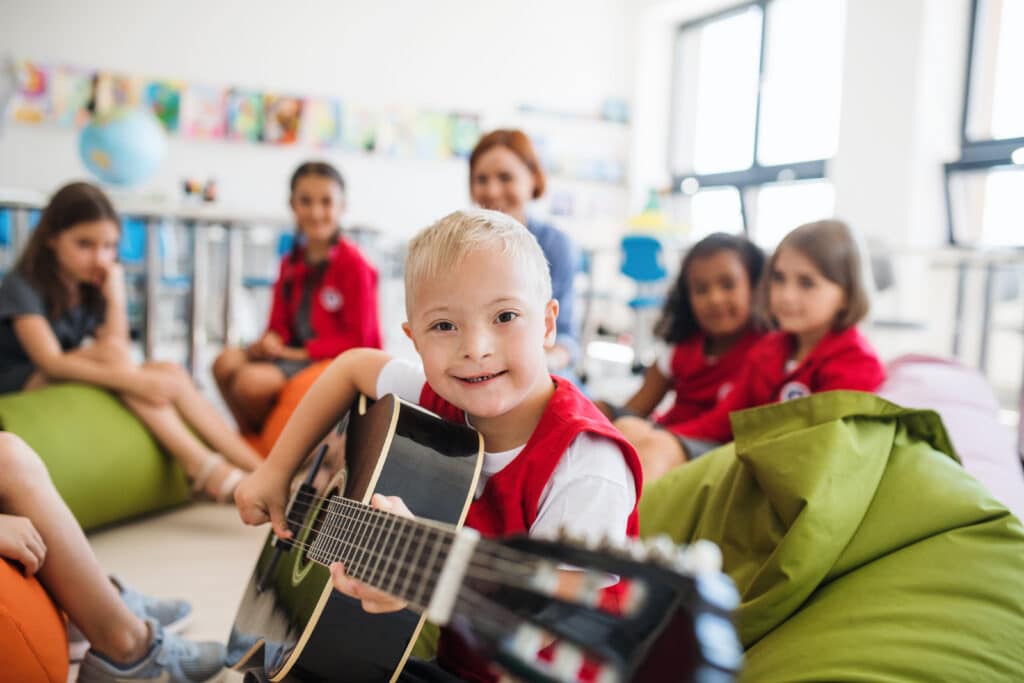 This boy is playing guitar at school where his disability inclusive education counts towards the Australian Disability Strategy statistics