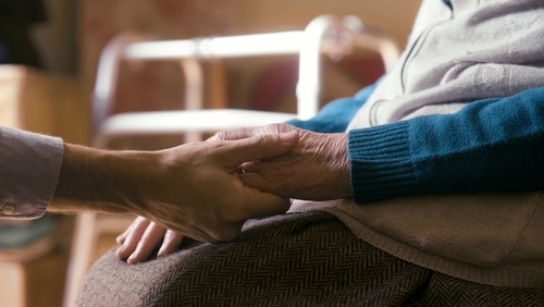 close up shot of an young man holding hands of a stroke survivor in wheelchair as sign of care and support.