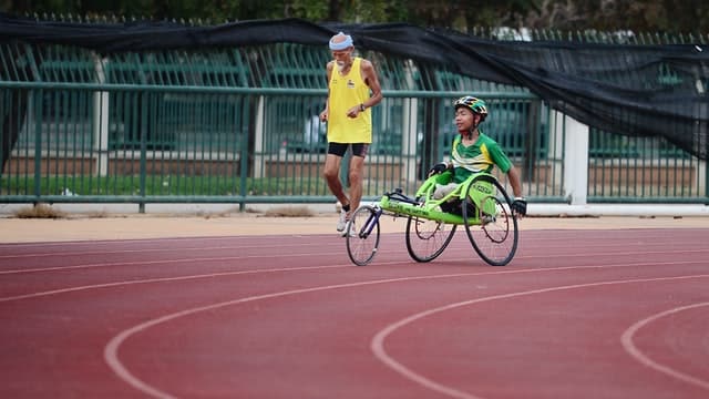 A boy spends time on the track with his coach who runs alongside him while he practices for disability inclusive competitions