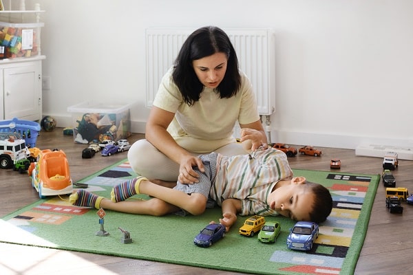 Child living with cerebral palsy (CP) entertaining on the mat with caregiver.