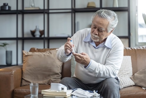 This is an image of an older man with diabetes in Australia sitting on his couch and injecting insulin into his finger. maybe he has type 2 diabetes