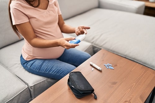 This is an image of a pregnant woman with gestational diabetes in Australia sitting on a couch and testing her blood sugar levels. 