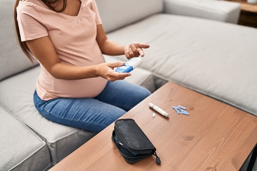 This is an image of a pregnant woman with gestational diabetes in Australia sitting on a couch and testing her blood sugar levels.