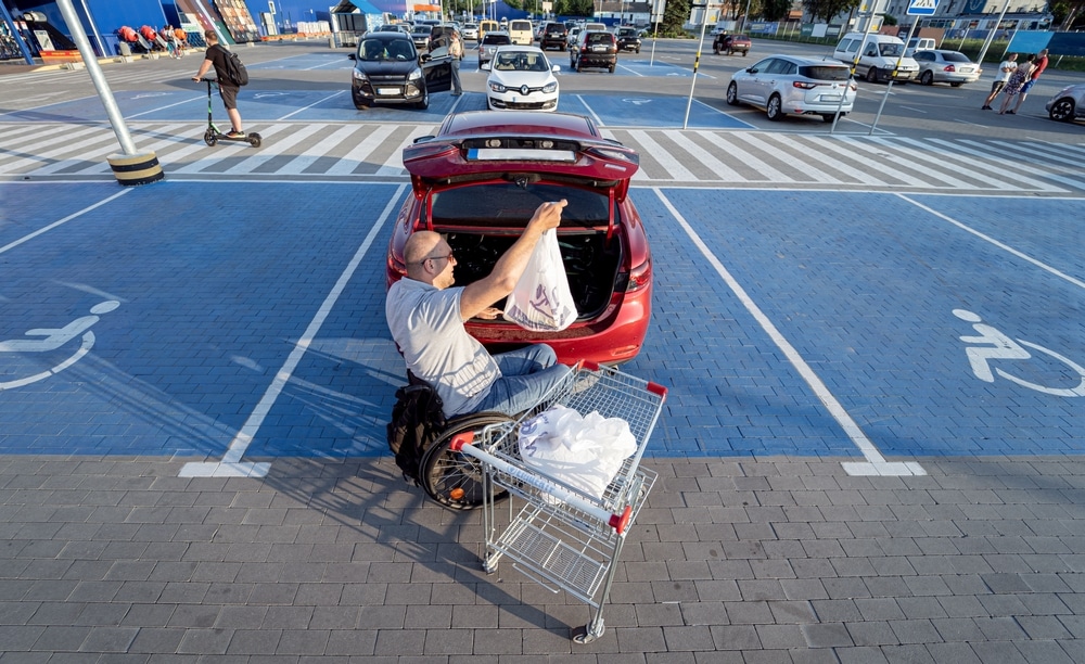 A man in a wheelchair loading a shopping cart in a parking lot where he can use priority parking thanks to successfully completing his application for an accessible parking permit