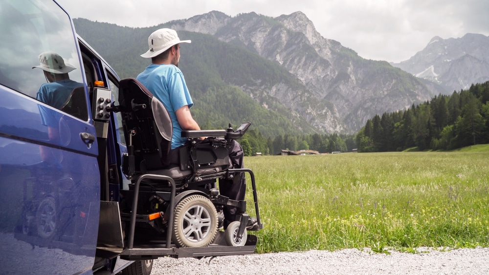 A man looks out at a vast mountainscape from his wheelchair accessible vehicle during a holiday roadtrip rest stop