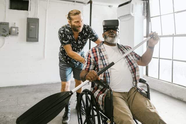 Two men engage in wheelchair exercises, with one man holding a paddle.