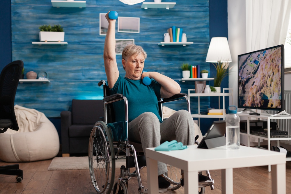 A woman in a wheelchair performing wheelchair exercises in her living room.