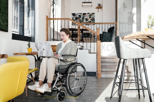 A woman who uses a wheelchair is researching disability car insurance discounts with Blue Badge Insurance on her laptop while having coffee at a cafe 