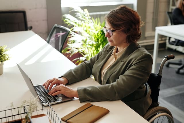 An entrepreneur with a disability efficiently operates a home business using a laptop in an office while seated in a wheelchair.