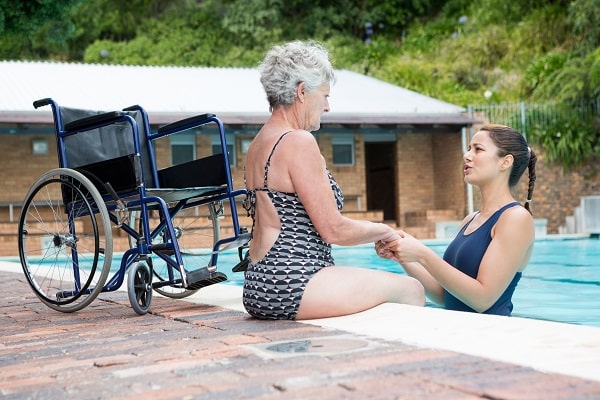 Swim coach consoling a disabled senior woman at poolside