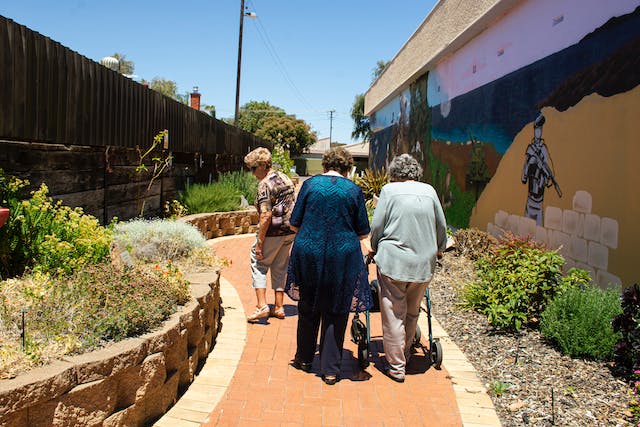 Australian seniors walking down a path with a mural, benefiting from CHSP and home care packages.