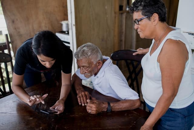 Australian seniors in an aged care facility sitting around a table, looking at a cell phone.