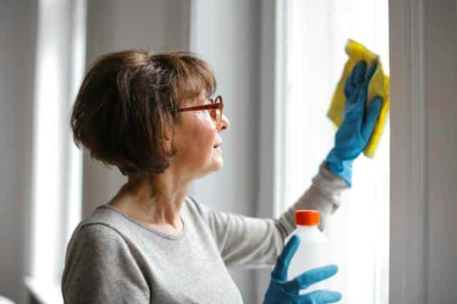 An aged care worker cleaning a window for a home care packages recipient.