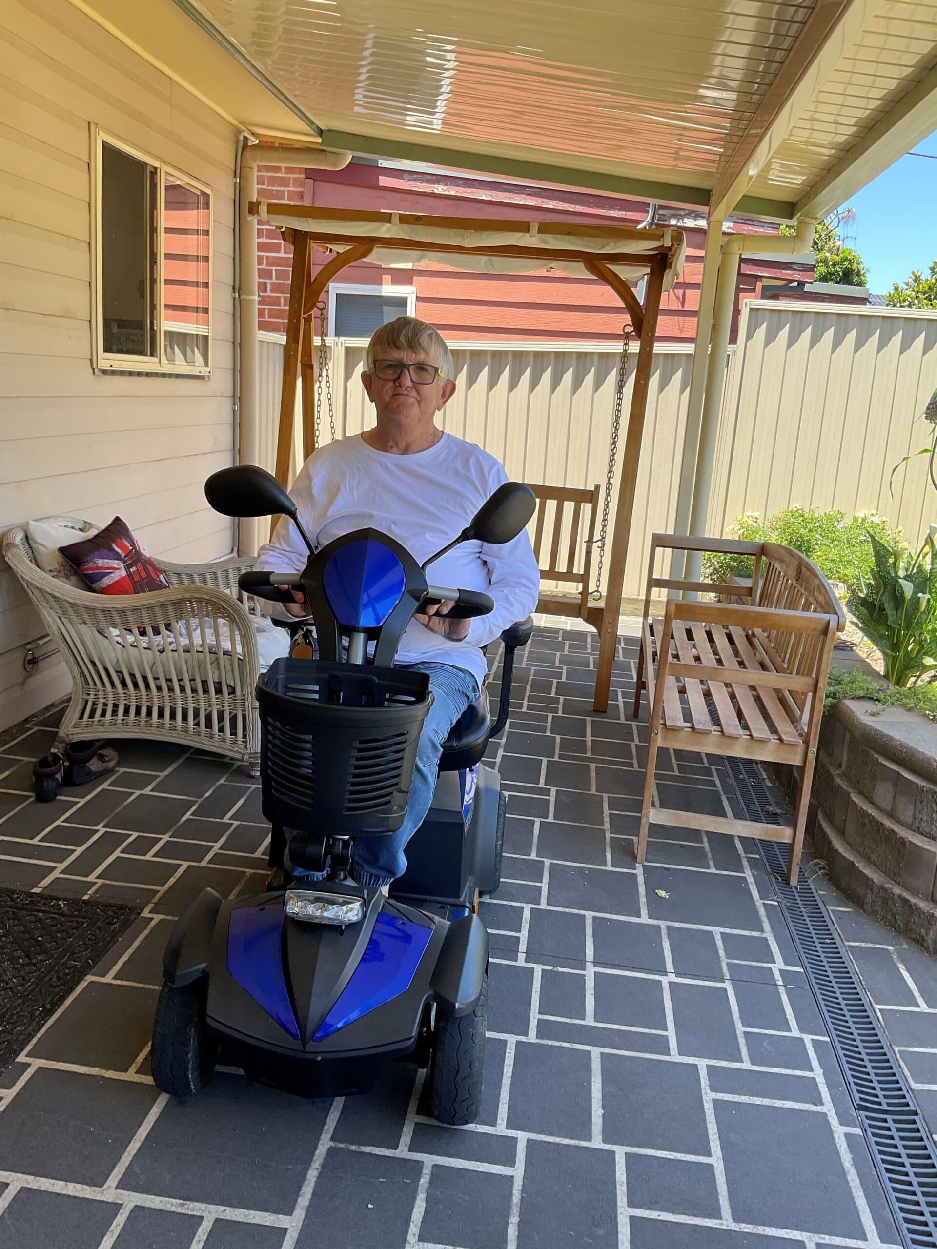 A man sitting on a motorized scooter in front of a house, inspecting mobility scooter parts.