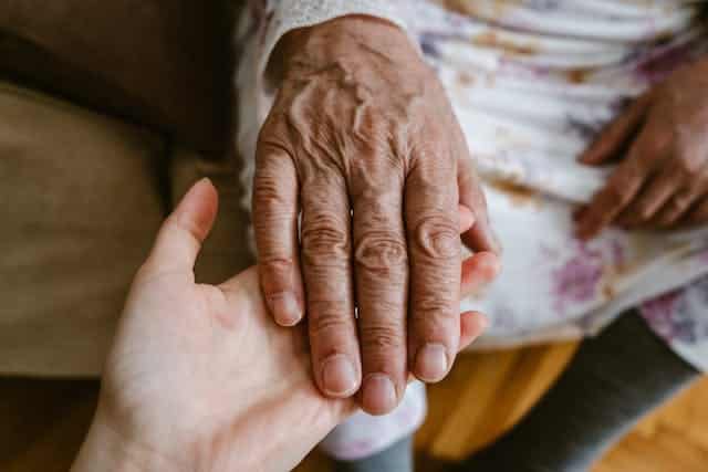 In Australia, a woman gently holds the hand of an elderly woman affected by arthritis.