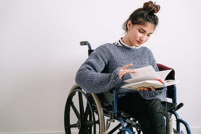 A woman in a wheelchair enjoying her book at home, covered by specialised insurance.