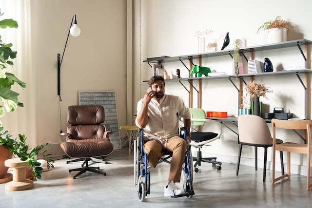After finding very little in the way of jobs for people with disability, this man has turned his own home business ideas into a profitable concept working out of his house, where he is pictures with pot plants and shelves on either side of his at-home office