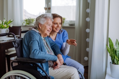 A nurse is helping an elderly woman in a wheelchair to prevent pressure sores.