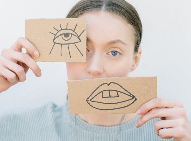 A woman demonstrating neurodiversity by holding up a cardboard with an eye and a mouth drawn on it placed slightly off-center.