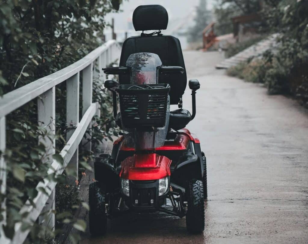 A red mobility scooter is parked on a bridge, after it stops working and is emitting beep codes.