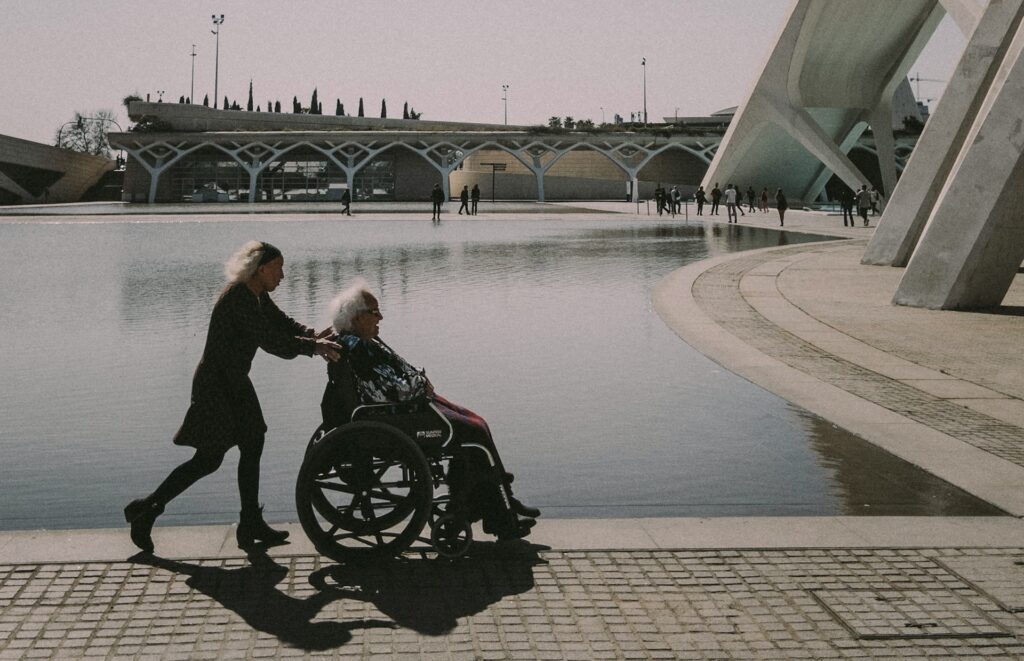 A woman pushes her husband who is currently receiving aged care funding in a wheelchair 