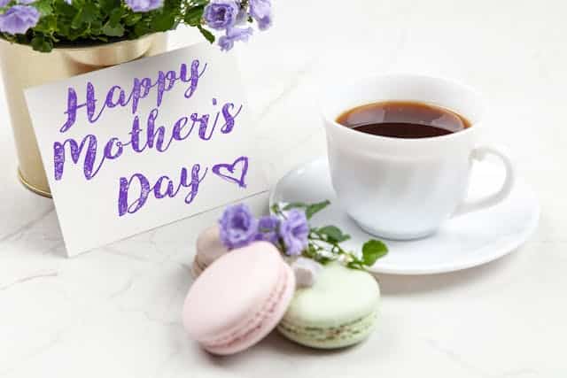 A cup of coffee and macaroons with a happy mother's day card.