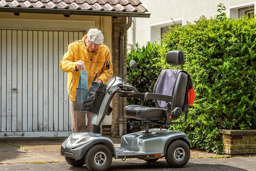 An elderly man on a mobility scooter in front of a garage.