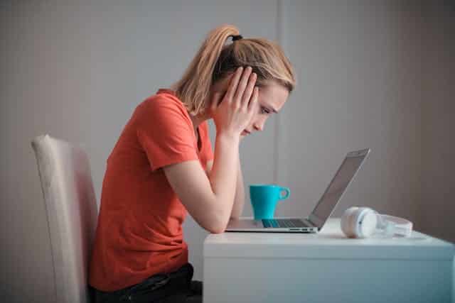 A woman with autism is sitting at a desk with a laptop and a cup of coffee, navigating her workplace struggles.