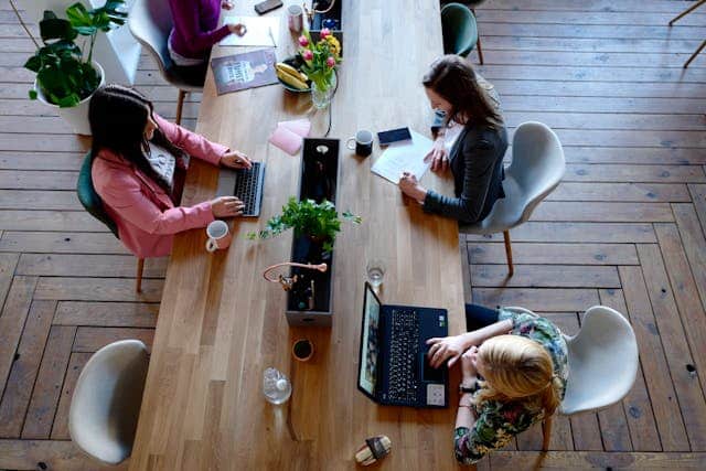 A group of women sitting at a table with laptops, navigating workplace struggles.