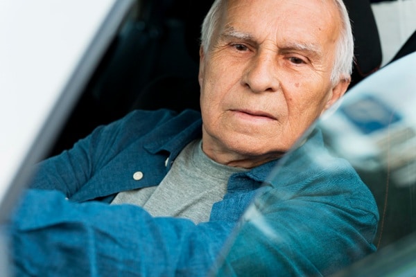 Older man with gray hair sits in the driver's seat of a car, looking out the window with a neutral expression, ready to get back on the road with support from a driver-trained occupational therapist.
