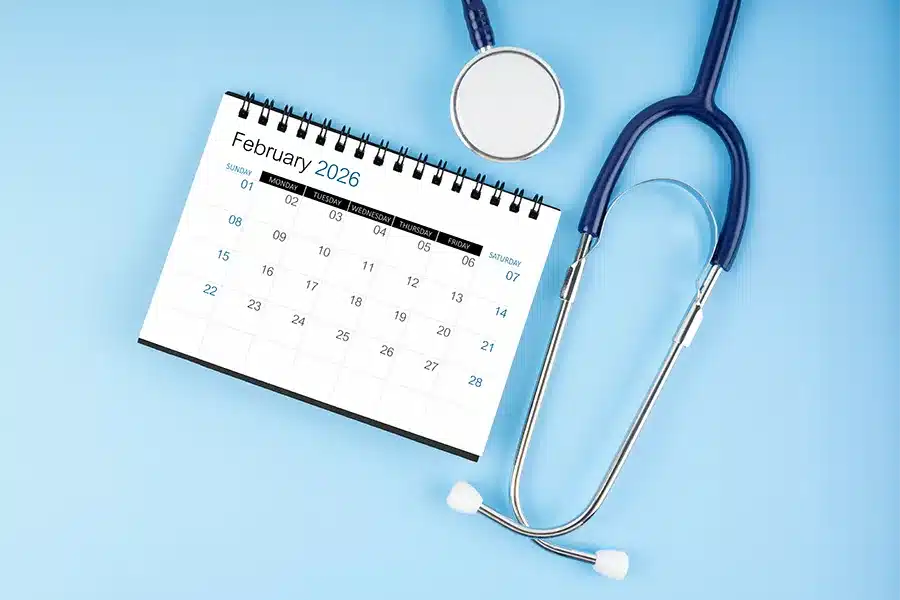 A February 2026 calendar sits on a blue surface next to a stethoscope, highlighting World Pet Health Month and the importance of pet wellness checkups.