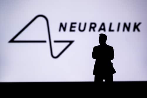 A person stands silhouetted in front of a large screen displaying the Neuralink logo and company name, highlighting the anticipation surrounding the Neuralink 2026 update.